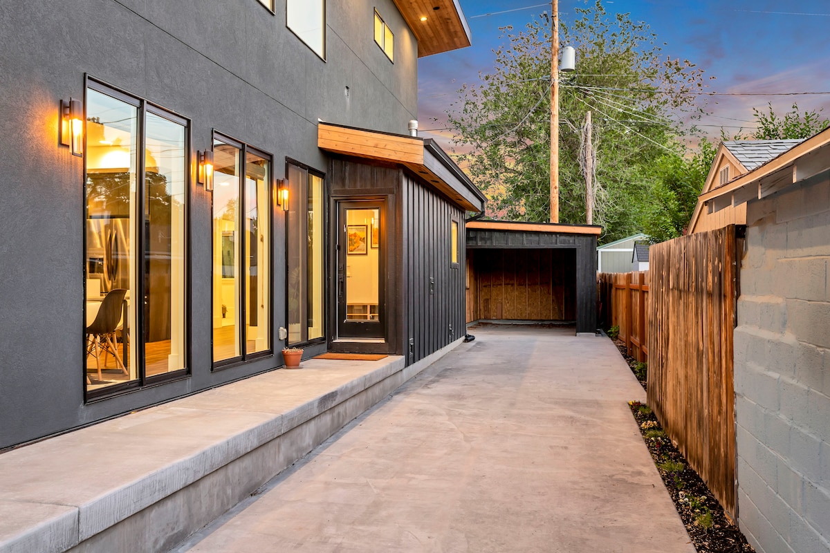The exterior of a two-story home features a modern design with large windows and warm outdoor lighting. A spacious concrete pathway leads to a separate entrance, with a well-maintained backyard and wooden fence providing privacy.