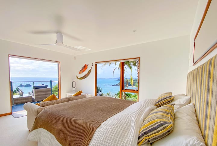 Dormitorio tamaño king con vistas al mar, sofá separado, terraza exterior y lujoso baño privado.