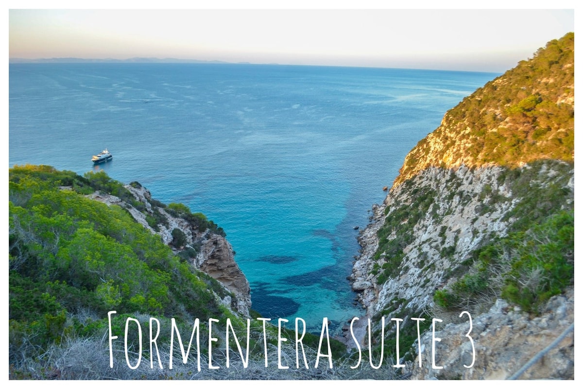 A coastal view reveals serene turquoise waters framed by rugged cliffs and lush greenery. A distant boat is visible on the horizon, contributing to the peaceful landscape that showcases the natural beauty of the area.