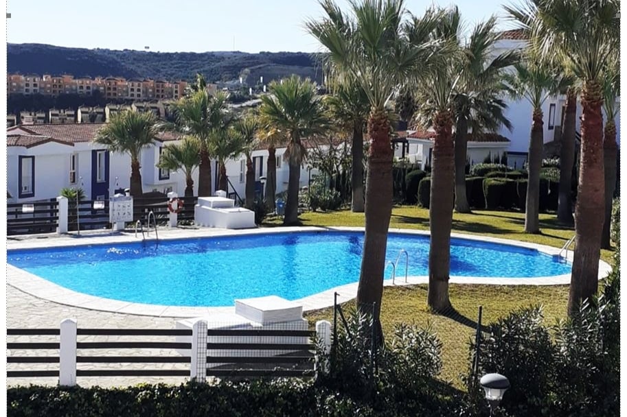 A large outdoor pool is surrounded by palm trees and well-maintained lawns. Sun loungers line the deck area, providing spaces for relaxation. The residential community is visible in the background, along with lush greenery enhancing the peaceful setting.