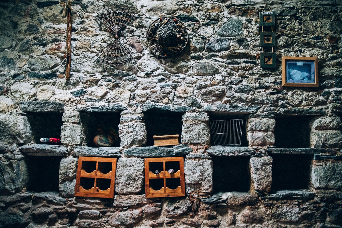 A rustic stone wall exhibits unique compartments that house various wooden frames and decorative items. The texture of the stones contrasts with the wooden accents, showcasing a blend of history and charm. Natural elements are subtly integrated throughout the arrangement.