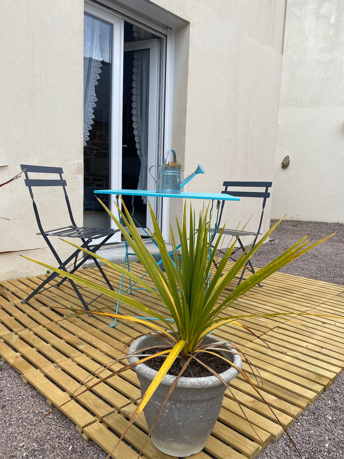 A private terrace is presented with a small round table and two metal chairs, inviting relaxation outdoors. A potted plant adds a touch of greenery, while the light wooden decking is visible underfoot. Nearby, a door opens to the interior space.
