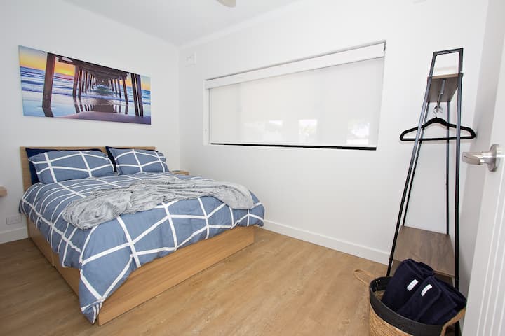 2ª camera da letto con tende oscuranti, ventilatore, letto matrimoniale, comodini con lampade, appendiabiti e specchio a figura intera sul retro della porta.