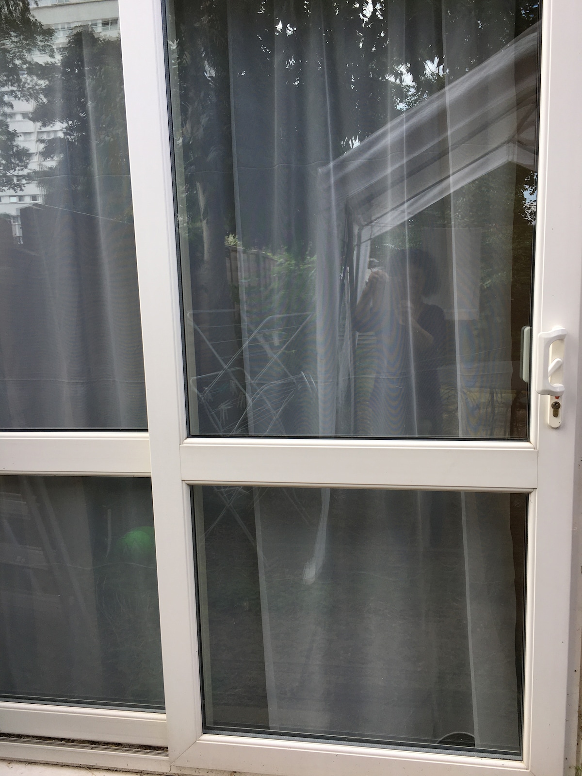 A sliding glass door is framed with white trim, featuring sheer curtains that softly filter light. The outdoor view reveals a glimpse of greenery, with an indication of a garden area visible beyond the door.