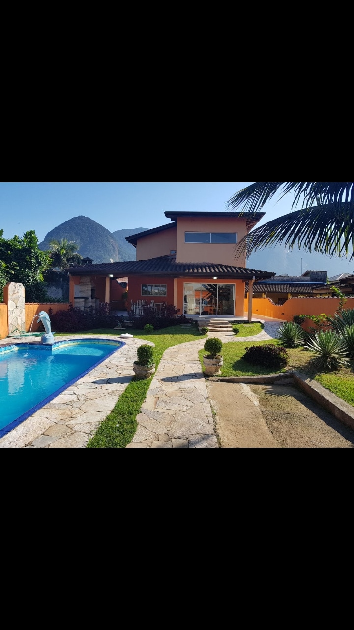 A two-story house is depicted, surrounded by lush greenery and featuring a private pool with a cascading fountain. The outdoor area includes a stone pathway leading to the entrance, with landscaped gardens and mountain views visible in the background.