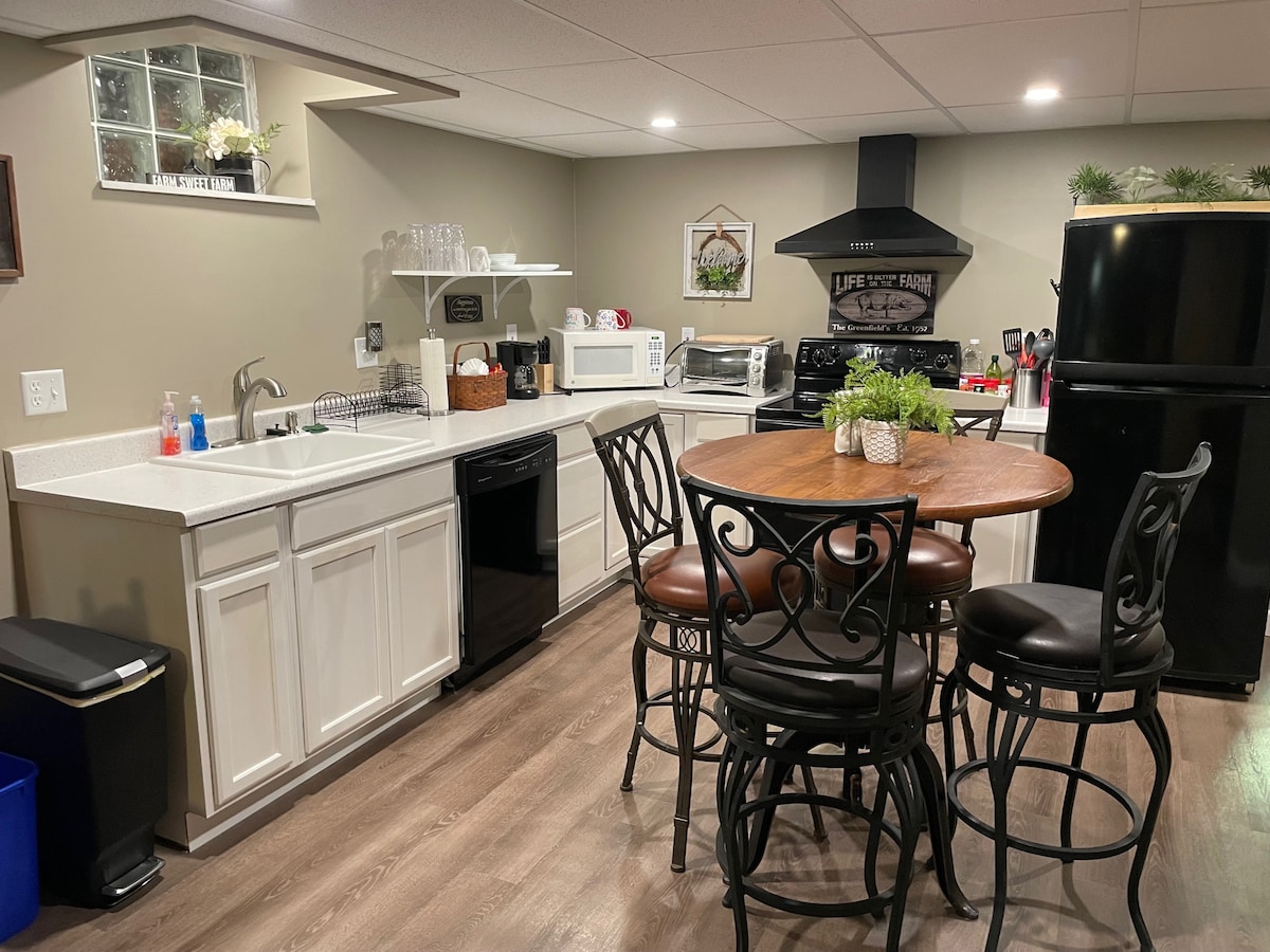 A well-equipped kitchen features white cabinetry, a sink, and a dishwasher. A round wooden table with four black metal chairs is positioned nearby. Essential appliances, including a microwave and refrigerator, are visible, contributing to a functional cooking space.