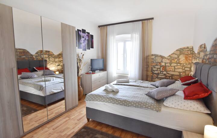 卧室配有一张双人床、两张带夜灯的床头柜、一个带镜子的衣柜和平板卫星电视