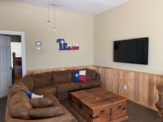 A cozy living area features a brown sectional sofa arranged around a wooden coffee table. A wall-mounted television is positioned opposite the seating, with a decorative Texas-themed wall art displayed nearby. Light-colored walls and wooden paneling add warmth to the space.