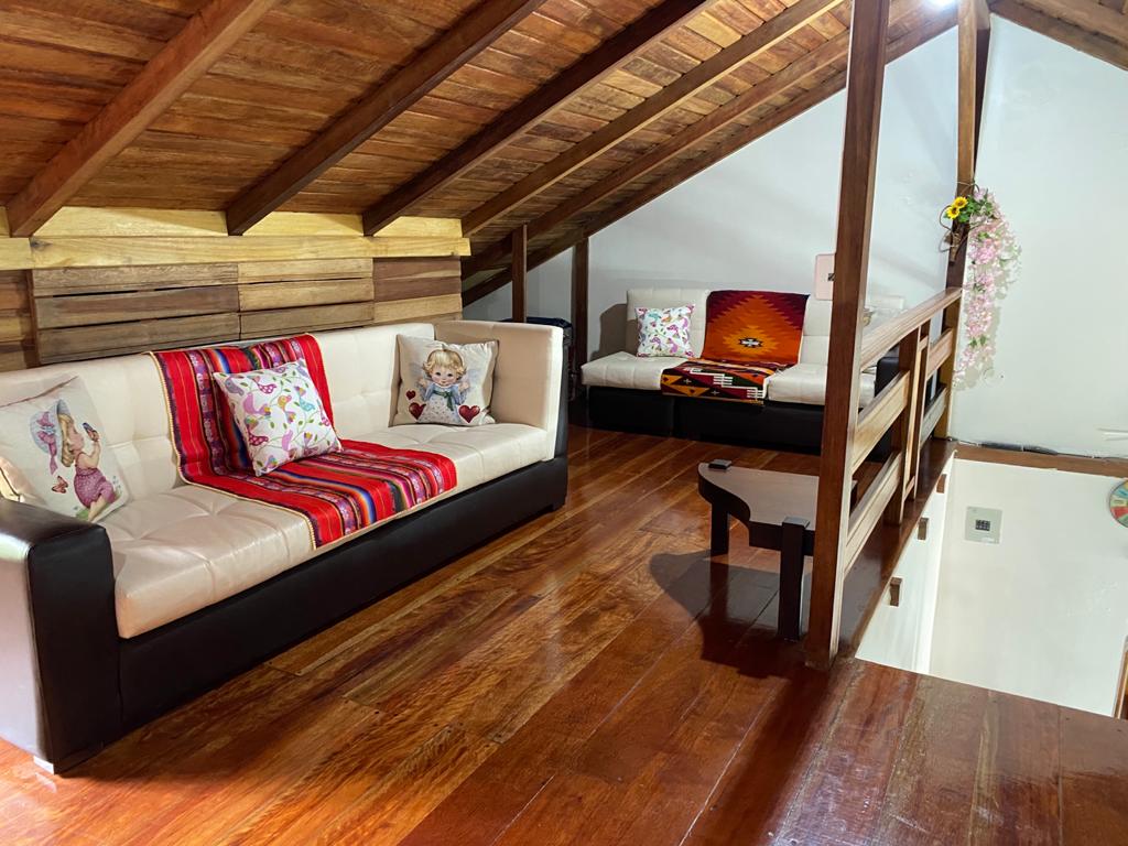 A cozy loft area is furnished with two comfortable sofas, featuring decorative cushions. The wooden ceiling showcases exposed beams, and the polished wooden floor enhances the warm ambiance. A small table is positioned nearby, creating an inviting space for relaxation.