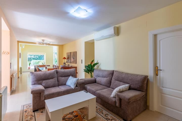 La sala cuenta con dos sofás grandes y cómodos de color gris, un mueble bajo con cajones y una mesa de centro de madera clara.