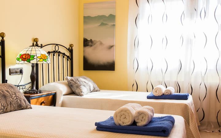 El dormitorio cuenta con dos camas individuales, vestidas con sábanas blancas y cobijas. 