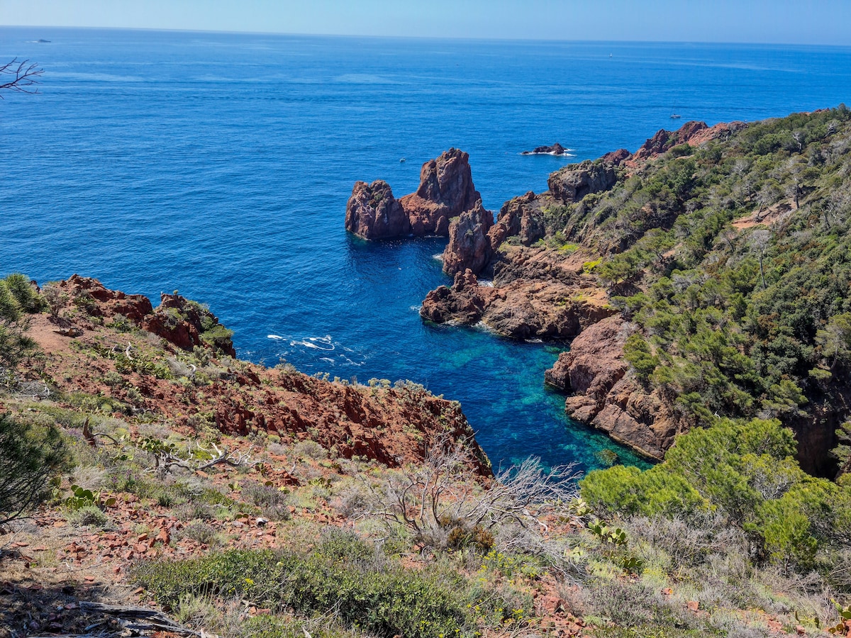 A stunning coastal view features rocky formations rising from clear blue waters. Lush greenery borders the shoreline, with steep cliffs leading down to the sandy beach. This serene natural landscape invites exploration and relaxation amid the vibrant colors of nature.