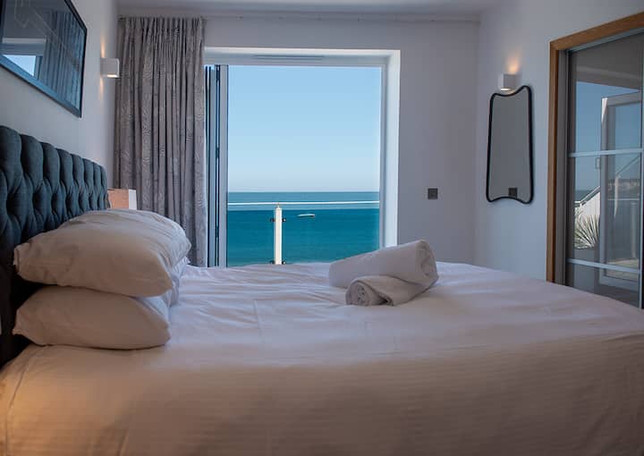 El dormitorio principal tiene vistas inigualables al mar, cama diván con colchón de bolsillo 2000 de calidad hotelera, armarios con puerta corrediza y su propio baño privado.