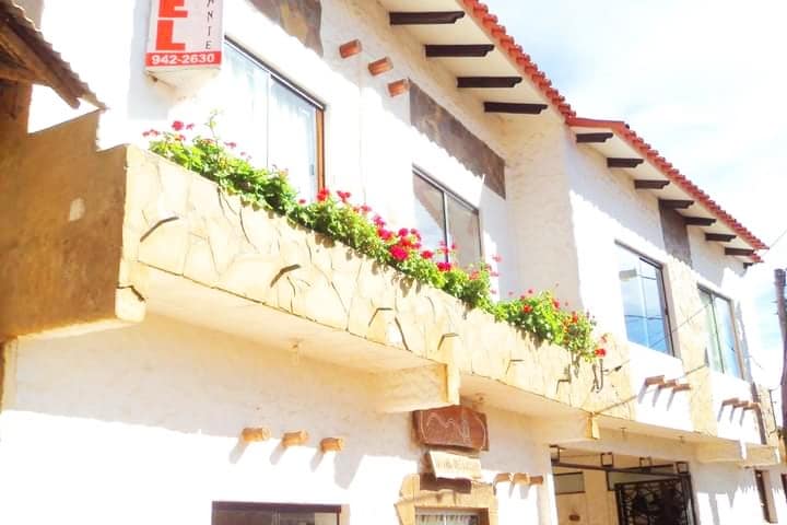 A two-story building features a light-colored facade accented by decorative stone elements. Flower boxes filled with vibrant blooms adorn the balconies, enhancing the inviting exterior. Large windows allow natural light to illuminate the spaces within.