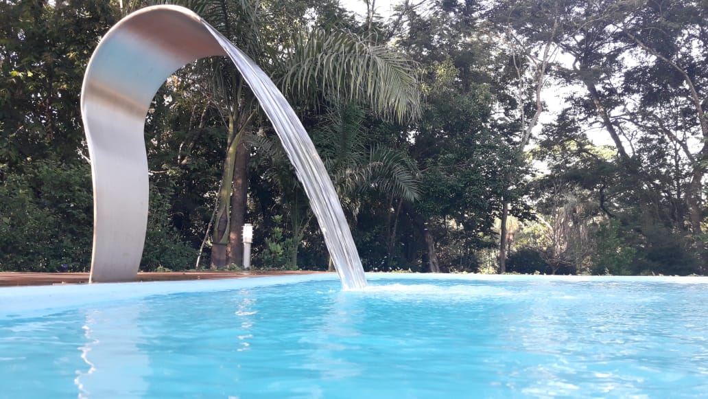 A private pool is showcased with a sleek, modern waterfall feature. The clear blue water complements the surrounding lush greenery, providing a serene outdoor space for relaxation.