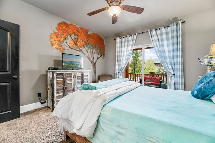 Bedroom 2, the master bedroom, features a king-sized bed, a "Scatter Kindness" slogan above the bed, a private balcony with a beautiful view, and a ceiling fan for added comfort—creating a serene retreat to relax and unwind.