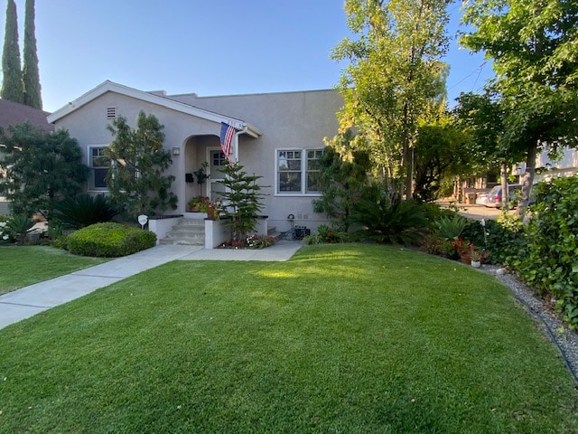 The exterior of the home is shown, featuring a well-maintained lawn and landscaped garden. A path leads to the welcoming entrance, adorned with potted plants and an American flag. Tall trees provide shade, enhancing the inviting front yard.