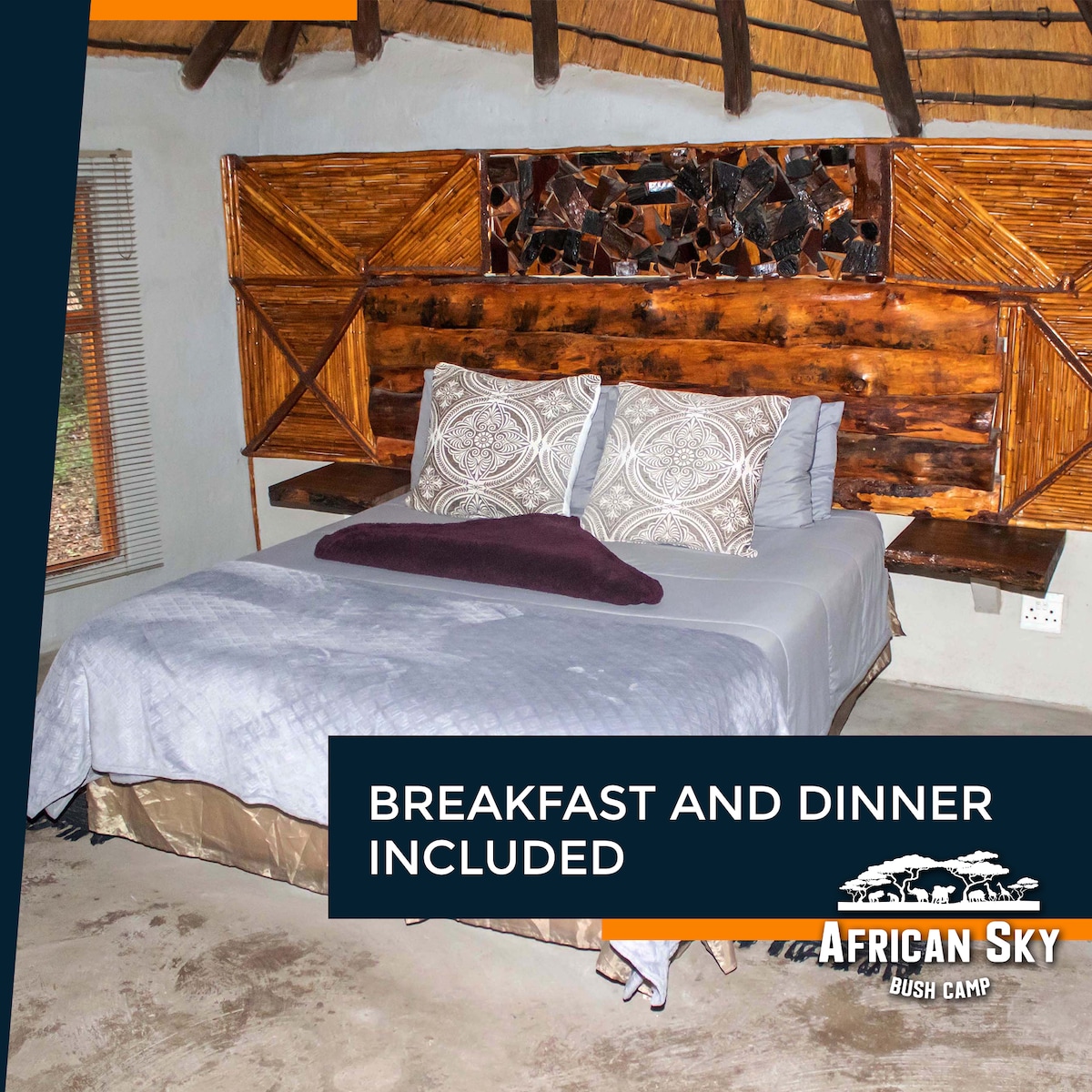 A cozy sleeping area is highlighted by a spacious bed with decorative pillows and a muted blanket. The room features natural wood accents and a unique headboard design. Soft lighting illuminates the space, complemented by textured walls and a window with woven blinds.