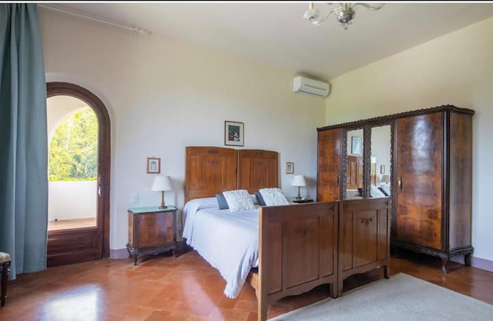 Relájate en este espacioso dormitorio principal con baño privado que ofrece una cama tamaño king, elegante mobiliario antiguo, aire acondicionado, terraza privada y vistas serenas al jardín para una estancia tranquila. 