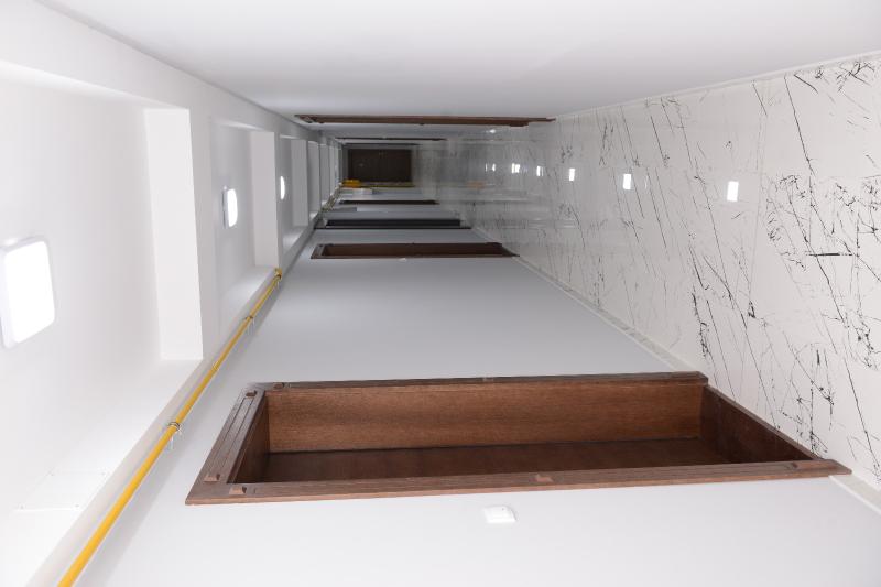 A long hallway is presented with smooth, glossy flooring and neutral-colored walls. Several door frames are aligned along the corridor, with light fixtures evenly spaced along the ceiling to provide illumination. An elegant marble accent wall adds a touch of sophistication to the space.