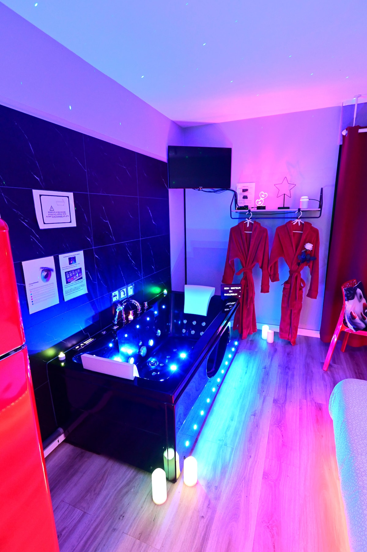 The spa area features a modern bathtub adorned with multicolored LED lights, creating a relaxing ambiance. Luxurious bathrobes hang on hooks nearby, and a flat-screen TV is mounted on the wall, providing entertainment options for guests.