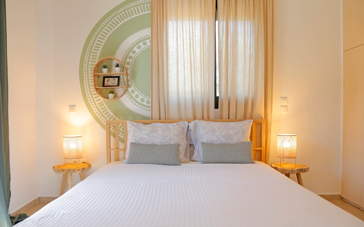 A spacious bedroom is showcased with a large bed featuring light linens and decorative cushions. Soft lighting from two bedside lamps creates a calming atmosphere. The light-filled space is complemented by a patterned wall and elegant window treatments.