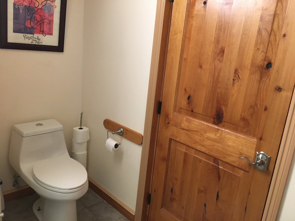 A well-maintained bathroom features a modern toilet positioned against a wall. Wooden elements are present in the door and trim, adding warmth to the space. A roll of toilet paper and an additional paper towel roll are conveniently placed nearby.