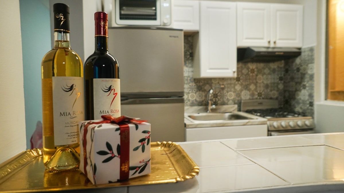 A well-equipped kitchen displays two bottles of wine, one white and one red, placed on a decorative tray alongside a wrapped gift. The modern appliances and tiled backsplash enhance the functional space.