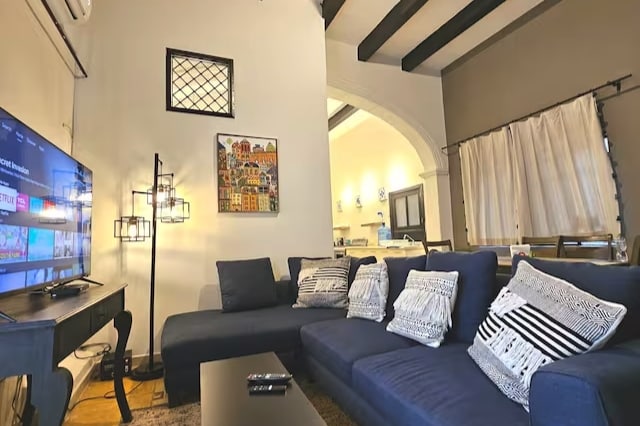 A spacious living area is furnished with a comfortable dark blue sofa adorned with decorative cushions. A black coffee table is positioned in front, while a large television is mounted on the wall. Soft lighting from a stylish floor lamp enhances the inviting ambiance.