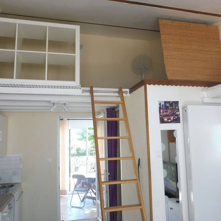 Стълба на първия етаж за достъп до мезанина от 6 кв. м, където има допълнително легло. Изгледи към мивката вляво и верандата пред мястото, където се намира кухнята