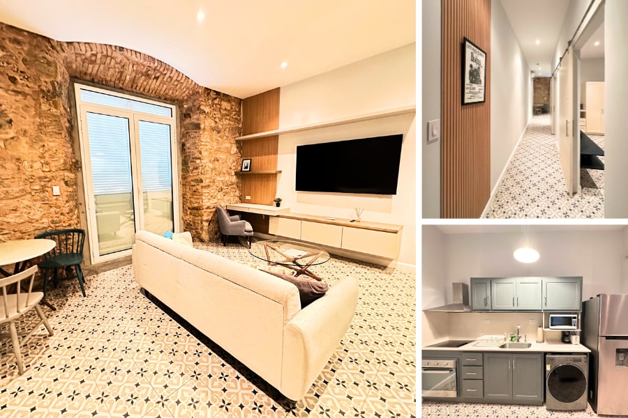 The living area features a comfortable sofa facing a large wall-mounted TV, with natural light filtering through expansive glass doors that lead to a balcony. The stylish floor tiles showcase a geometric pattern, enhanced by the antique calicanto walls that add character.