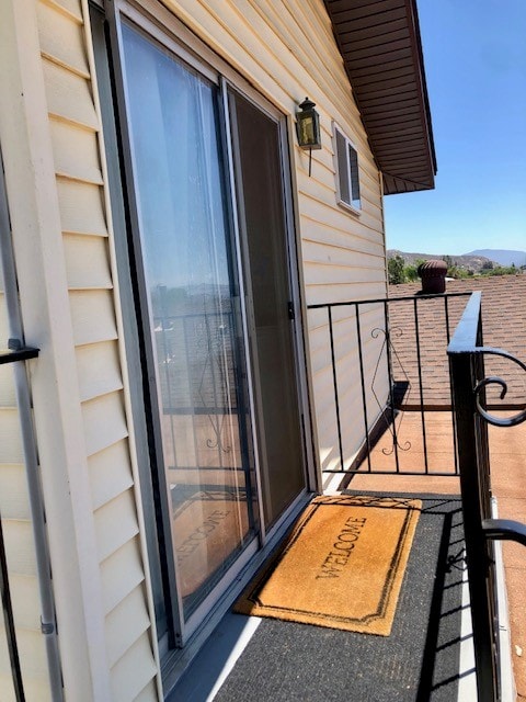 An outdoor space features a welcome mat placed at the entrance to the unit, with a glass sliding door leading inside. A wrought iron railing provides safety and an unobstructed view of the surrounding landscape, including distant mountains and clear blue skies.
