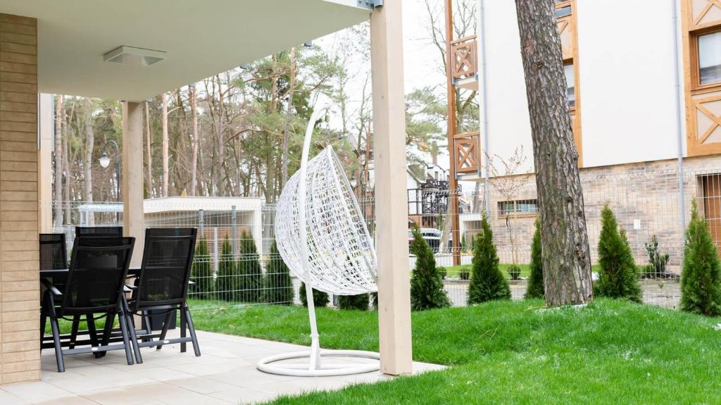 A covered outdoor area includes a hanging chair and a dining table with six chairs. Lush green grass surrounds the space, while trees and a fenced area provide a sense of privacy. The setting is conducive to relaxation and outdoor dining.