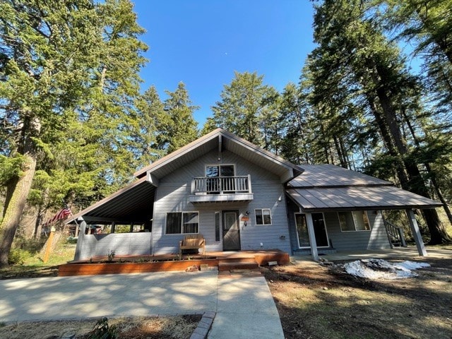 The exterior of a spacious woodsy home is presented, featuring multiple gabled roofs and a covered entryway. A large deck extends from the front, and a balcony is visible on the second floor. Surrounding pine trees enhance the natural setting.