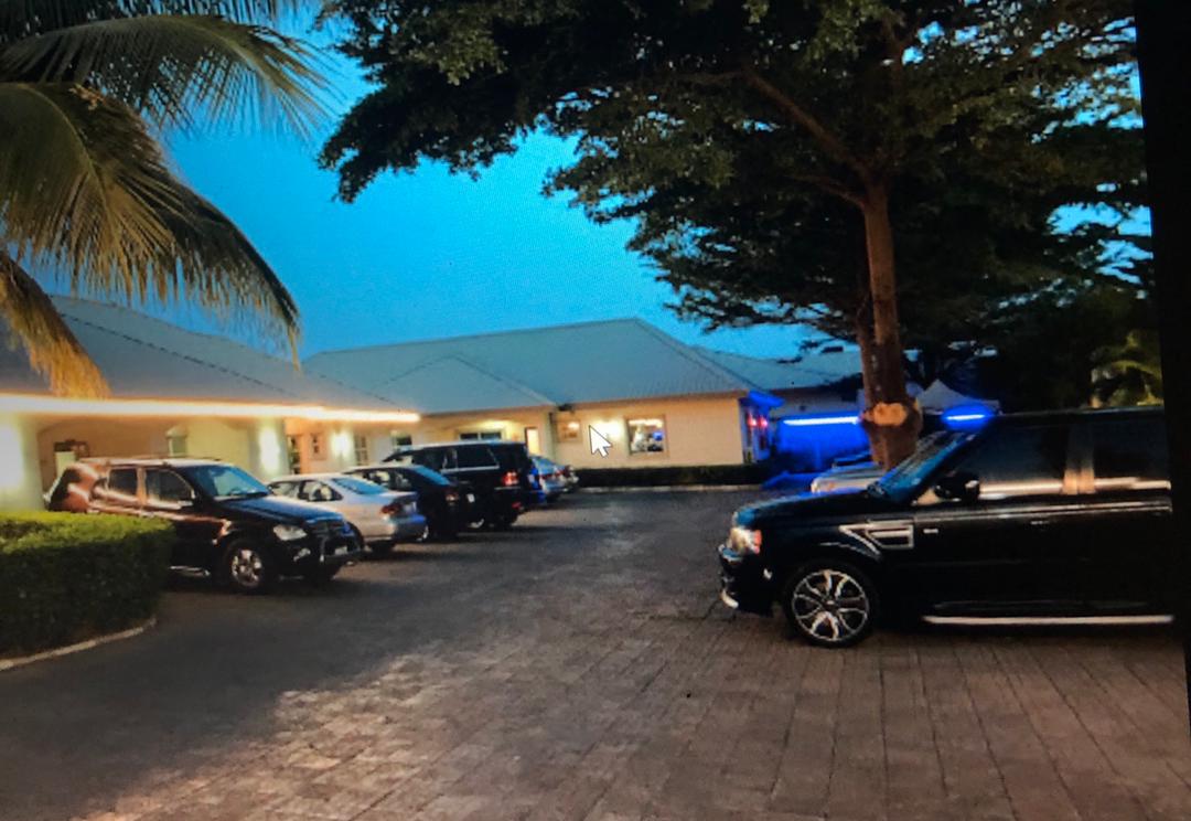 A spacious parking area features several parked vehicles, including SUVs and sedans. Lush green landscaping borders the lot, with tall trees providing shade. Soft evening light casts a gentle glow over the surroundings, accentuating the accessibility of the space.