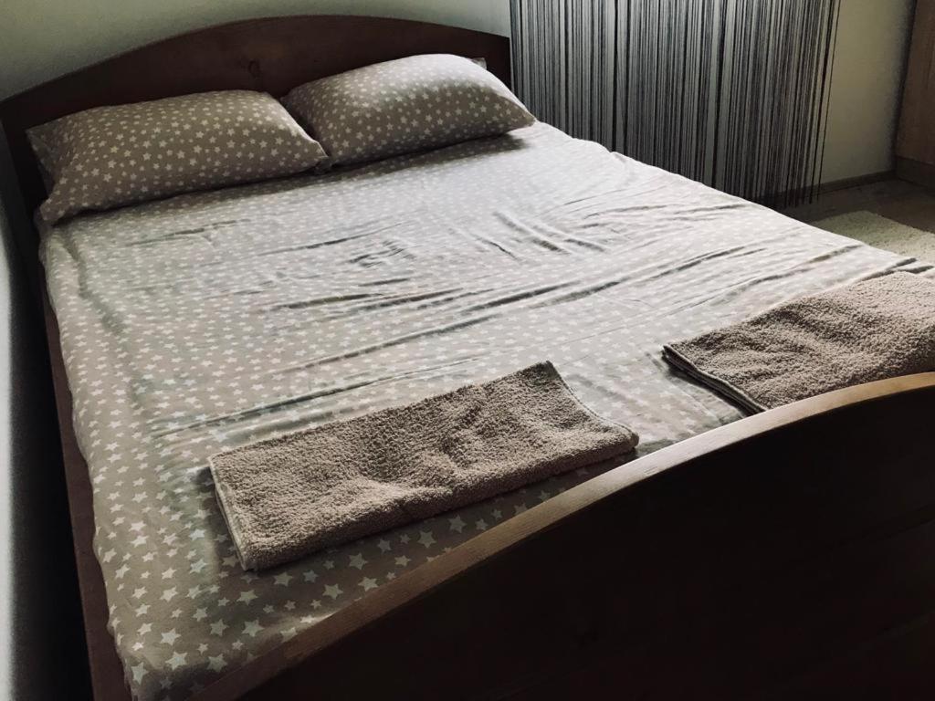 A spacious bed is dressed in a light grey star-patterned cover with two matching pillows. Two folded towels are neatly placed at the foot of the bed. The backdrop features soft, flowing curtains that provide a sense of privacy.