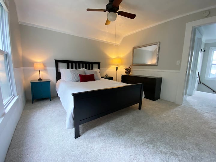 The larger upstairs bedroom features a queen bed, six-drawer dresser, two bedside tables, and a spacious closet.