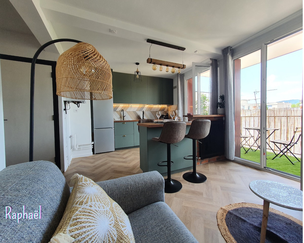 A modern kitchen space is highlighted with a central island and stylish barstools. Large windows provide natural light and a view of a balcony, where outdoor seating is arranged. A comfortable sofa adds a cozy touch to the open living area.