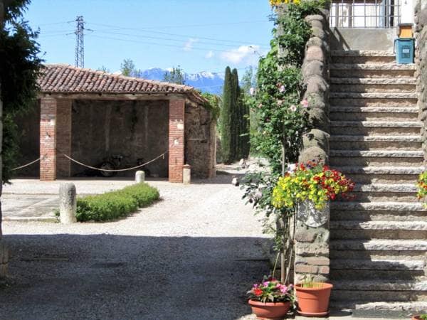 A private entrance leads to a charming outdoor area featuring a stone staircase adorned with vibrant flower pots. The scenic view includes a rustic structure on the left, with mountains visible in the distance under a clear blue sky.