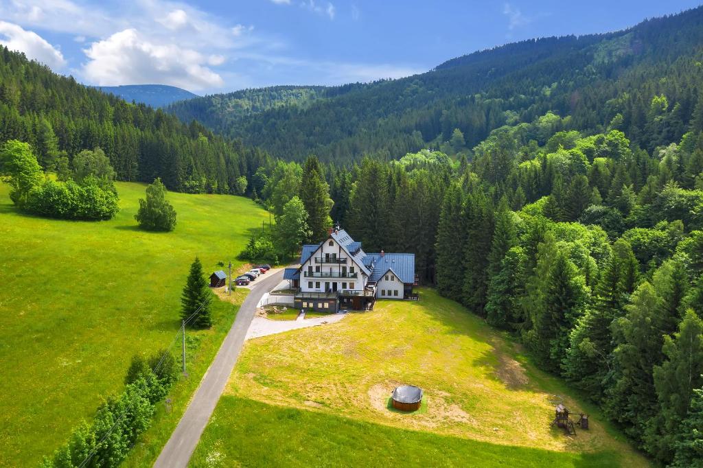 The image captures a spacious mountain lodge nestled within a green landscape, surrounded by trees. A gravel driveway leads to the building, with parking visible. The lodge features a mix of dark and light exterior, complementing the natural beauty of the area.