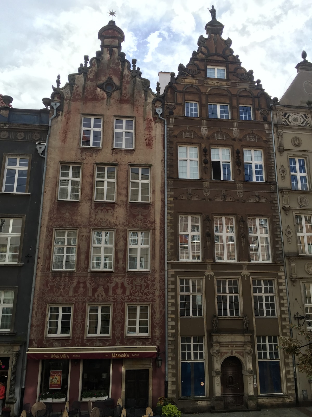 Three historic buildings are showcased in a row, highlighting architectural details such as ornate facades and decorative elements. The left building features faded red textures, while the central and right buildings exhibit contrasting color schemes and structural embellishments, creating a visually engaging streetscape.