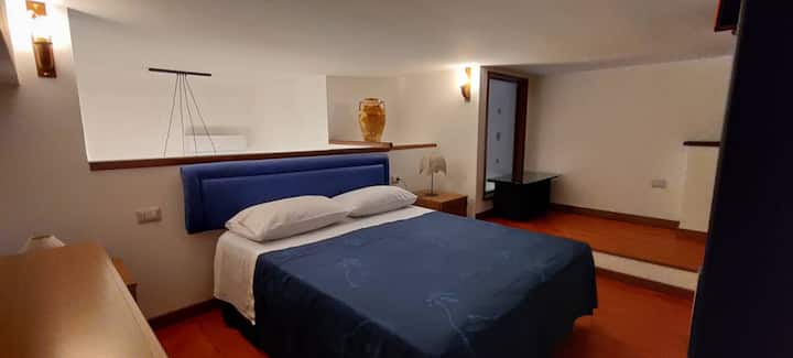 Chumba cha kulala kwenye sakafu ya roshani ya mbao: kitanda cha ukubwa wa malkia, na ubao wa kichwa na meza za kitanda - mtazamo wa panoramic O/E