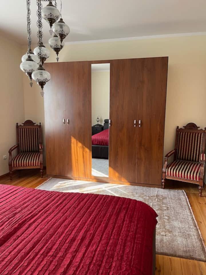 Chumba kikubwa cha kulala chenye nafasi kubwa (21sq.m) kina kitanda kikubwa cha ngozi, meza mbili za kando za kitanda, kabati lenye ukubwa maradufu, viti viwili vya mikono na rafu iliyofungwa.