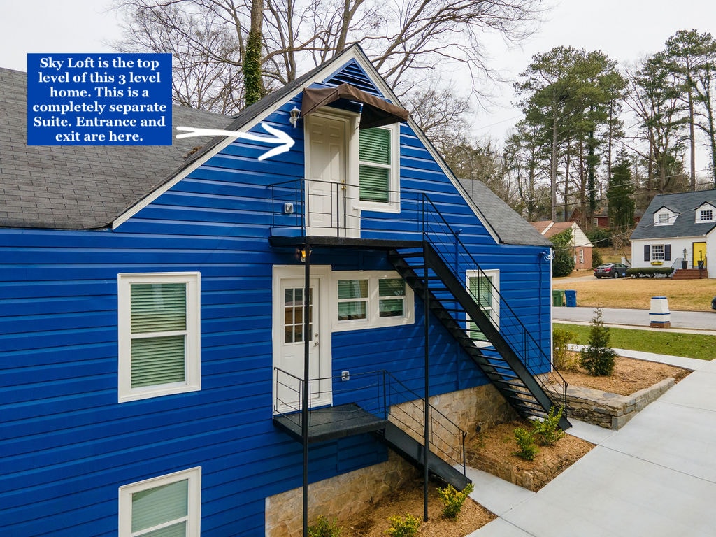 The exterior of the building features a vibrant blue façade, highlighting the unique architectural design. A prominent fire escape-style staircase leads to the top level suite, which is marked by a private entrance. Surrounding landscaping is neatly maintained with a pathway visible.
