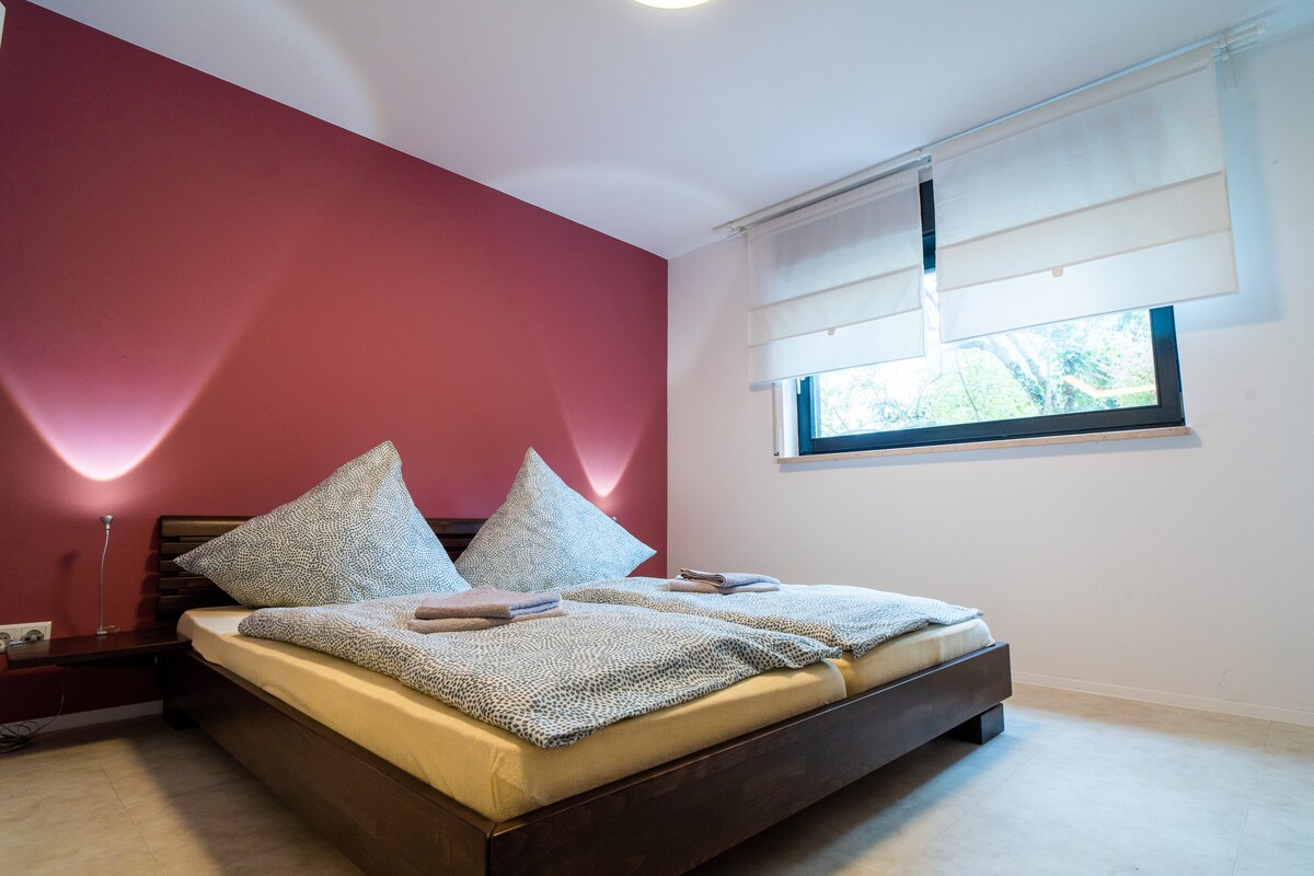 ห้องนอนเสริมที่มีหน้าต่างขนาดใหญ่ในเวลากลางวันและมีพื้นที่สีเขียว/ธรรมชาติมากมายอยู่ด้านนอก