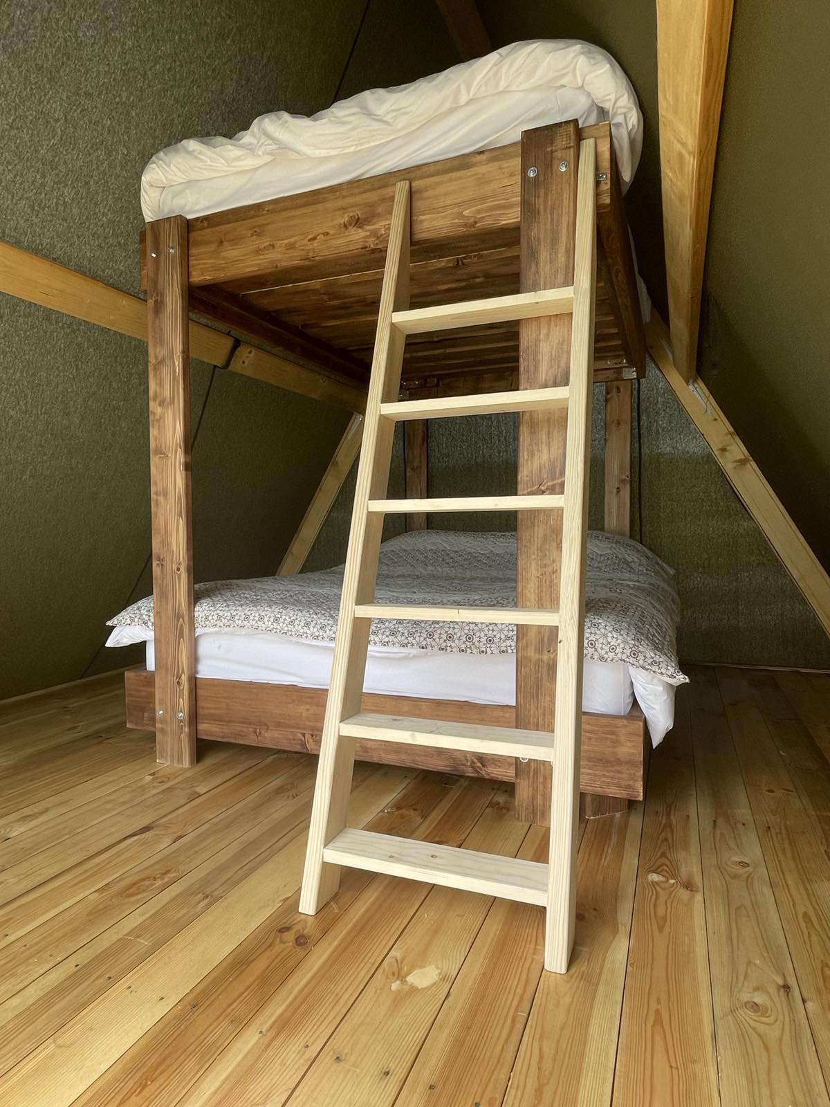 A serene sleeping area features a wooden bunk bed, with a top mattress neatly made. A ladder leads to the upper bunk, while a spacious bed below is adorned with light bedding. Natural wood flooring complements the warm tones of the interior.