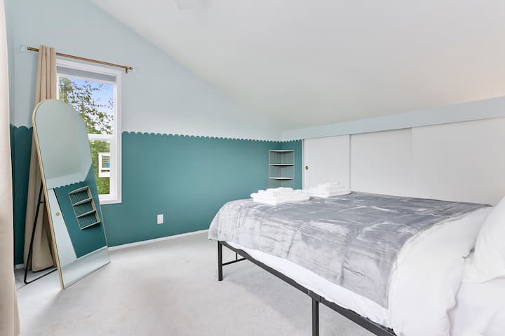 Spavaća soba u potkrovlju na katu s bračnim krevetom i ogledalom pune veličine, pružajući vam najbolji pogled na jezero u cijeloj kući. 