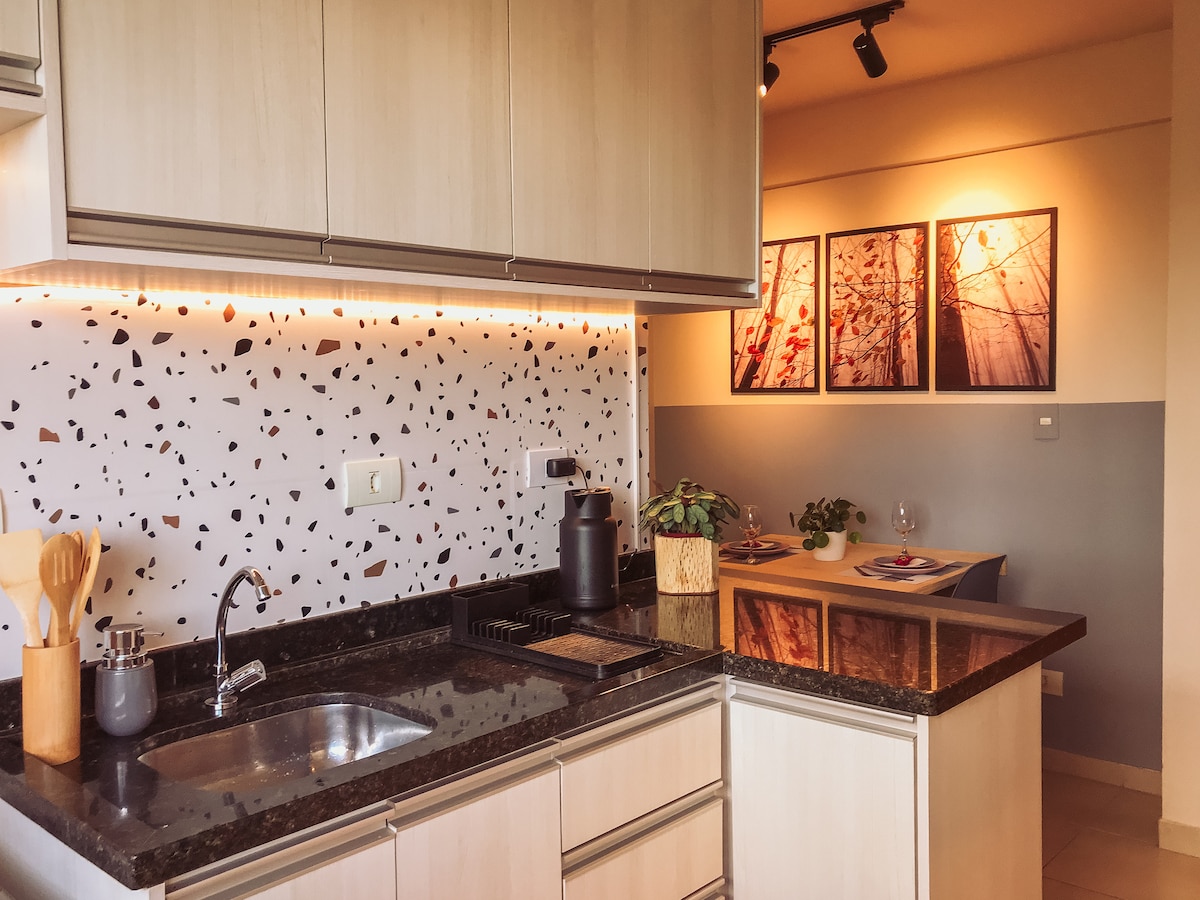 The kitchen area features modern cabinetry and a dark granite countertop, complemented by a distinctive backsplash of patterned tile. Above, subtle lighting highlights framed artwork, while a dining table is set for two, creating a welcoming space for meals.