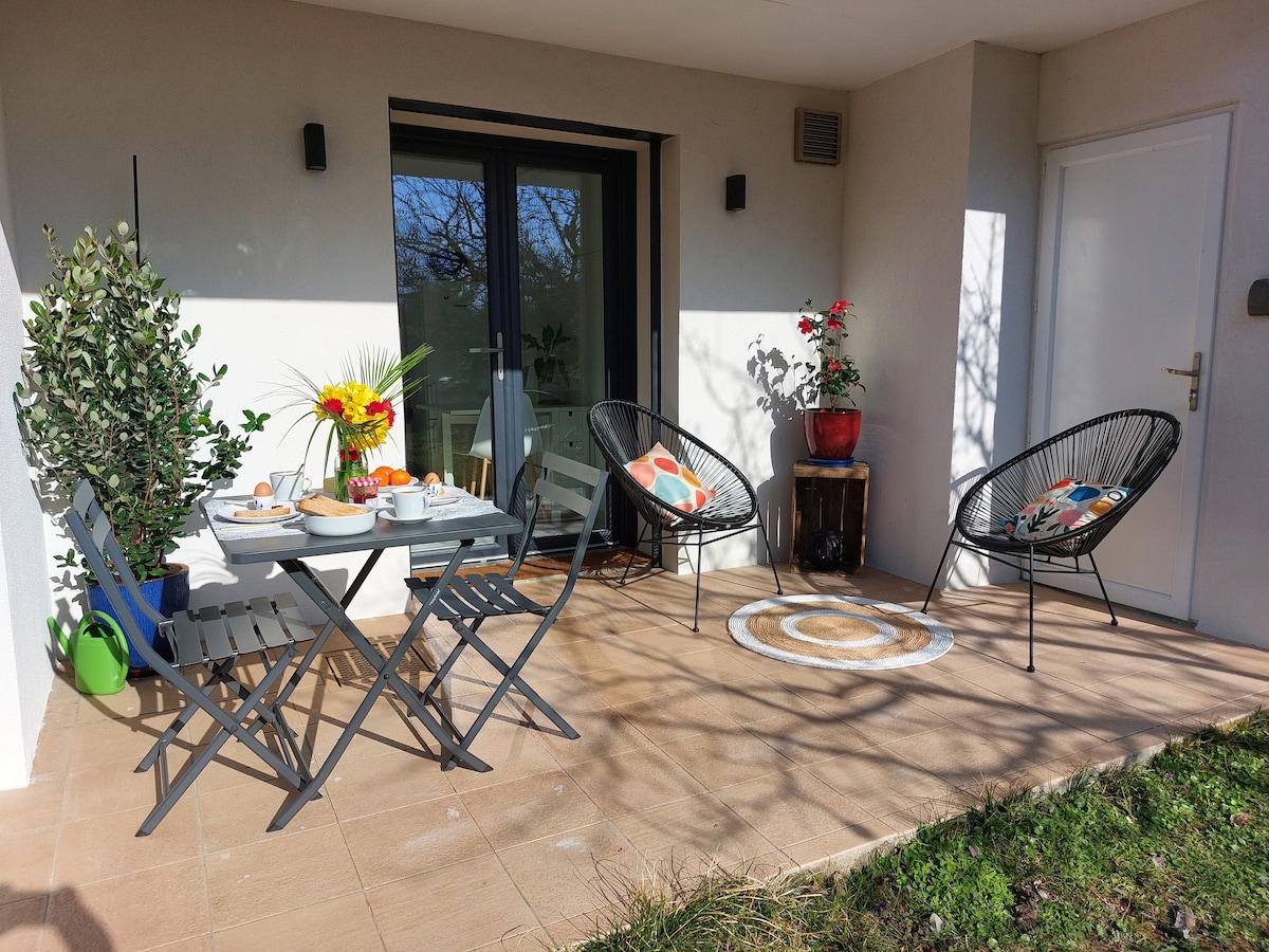 A welcoming patio area is featured, highlighting a small dining table set for two and two stylish chairs. Potted plants add greenery, and a decorative rug is placed on the tiled floor. Natural light filters in, creating an inviting outdoor space.