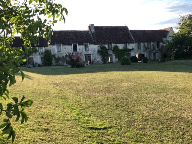 The spacious exterior of a historic building is displayed, featuring a stone facade adorned with climbing greenery. A well-maintained lawn extends in front, creating an inviting outdoor area. The soft glow of evening light highlights the architectural details and surrounding natural landscape.